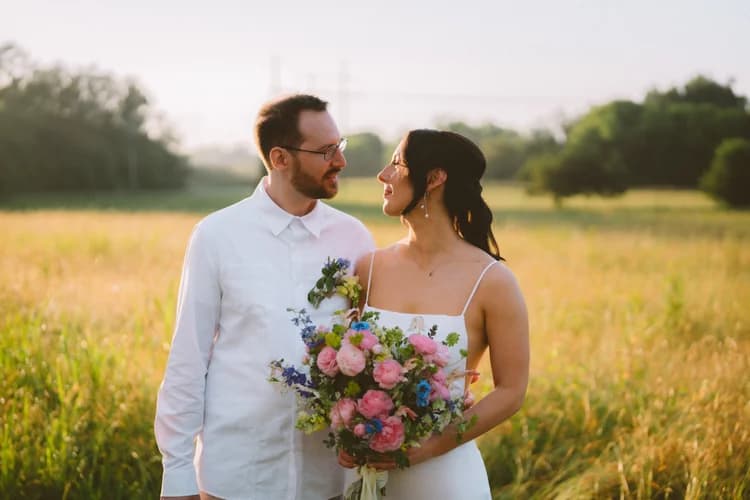 Couple walking through a golden grass field with a bouquet